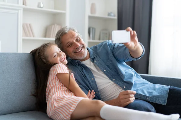 Un selfie divertido con papá. Autorretrato del padre y su hijita tomando selfie mientras están sentados en el sofá. — Foto de Stock