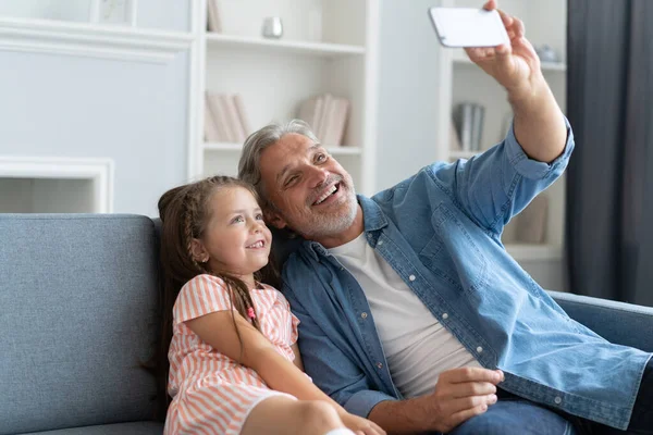 Un selfie divertido con papá. Autorretrato del padre y su hijita tomando selfie mientras están sentados en el sofá. — Foto de Stock