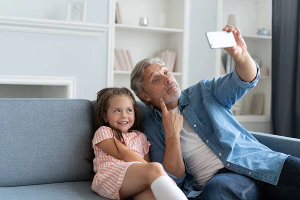 Grappige selfie met papa. Zelfportret van vader en zijn dochtertje selfie terwijl ze op de bank zitten. — Stockfoto