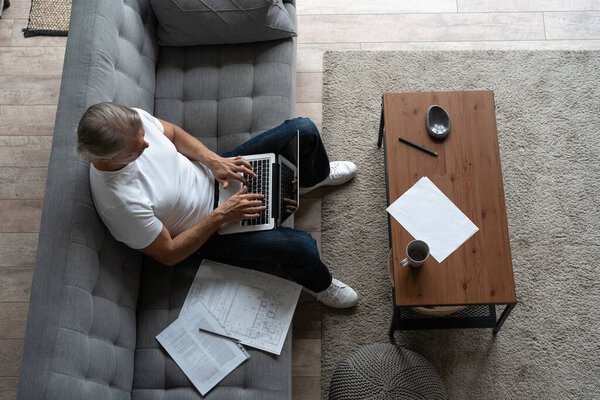 Мужчина среднего возраста работает из домашнего офиса на ноутбуке.