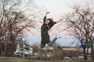 Mutluluk ve özgürlük kavramı. Güzel şık genç Avrupa kadın modeli trendy hoodie ve beyaz sneackers giymiş uzun kahverengi saçlı açık portresi saatler, akşam sonbaharda atlama veya