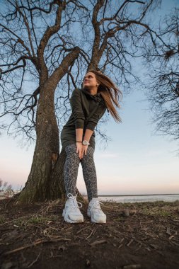 Kentsel stil ve moda kavramı. Güzel şık genç Avrupa kadın modeli trendy hoodie ve beyaz sneackers giymiş uzun kahverengi saçlı açık portresi saatler, akşam sonbaharda poz veya