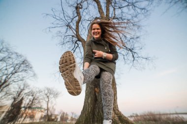 Kentsel stil ve moda kavramı. Güzel şık genç Avrupa kadın modeli trendy hoodie ve beyaz sneackers giymiş uzun kahverengi saçlı açık portresi saatler, akşam sonbaharda poz veya