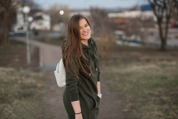 Estilo urbano y concepto de moda. Retrato al aire libre de hermosa elegante modelo femenino joven europeo con el pelo largo marrón con sudadera con capucha de moda y zapatillas blancas relojes, posando en la noche de otoño o — Foto de Stock