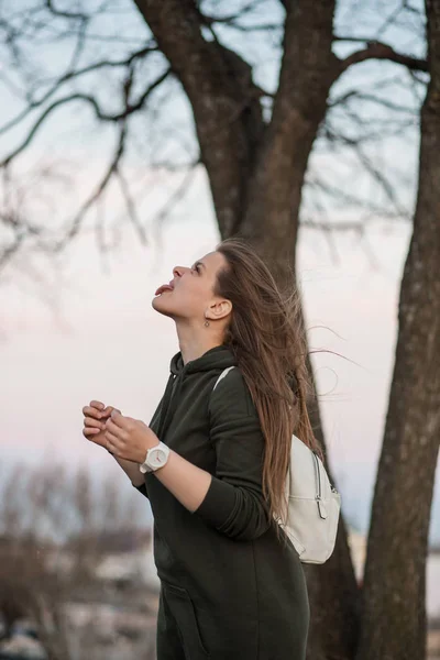 Estilo urbano y concepto de moda. Retrato al aire libre de hermosa elegante modelo femenino joven europeo con el pelo largo marrón con sudadera con capucha de moda y zapatillas blancas relojes, posando en la noche de otoño o — Foto de Stock