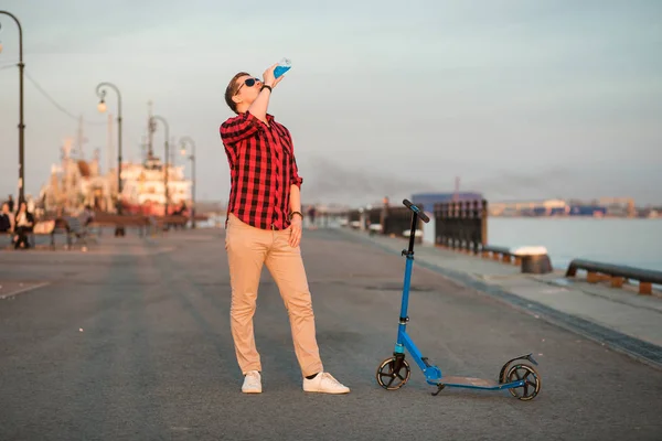 Agradable hombre bebiendo bebida isotónica azul y posando con patada azul scooter — Foto de Stock