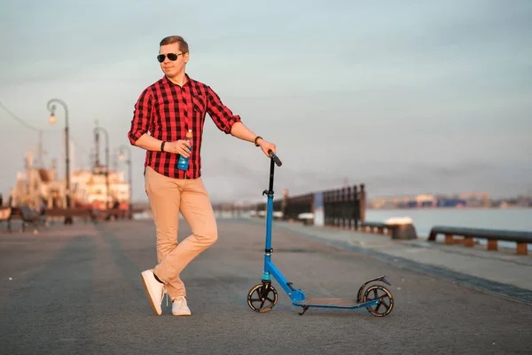 Agradable hombre sonriente posando con patada azul scooter y botella de bebida isotónica azul — Foto de Stock