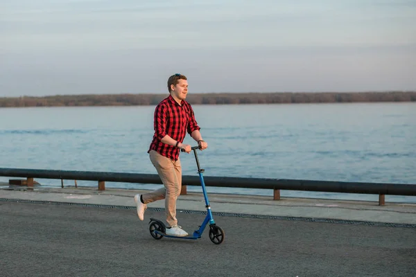 Junger Hipster-Mann, der nach der Arbeit bei Sonnenuntergang auf einem Tretroller fährt. Konzept eines gesunden mobilen Verkehrs — Stockfoto