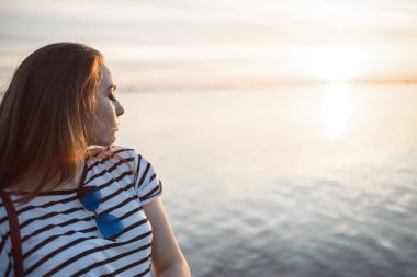 Genç bir kadın günbatımında bir deniz veya nehir üzerinde su güzel yumuşak güneşli yansımaları ile arıyor