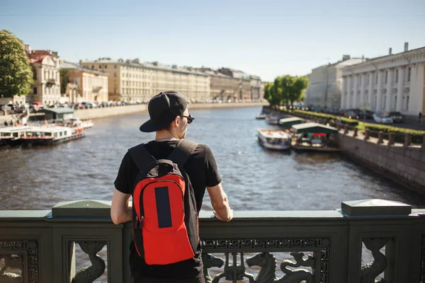 Elegante turista masculino com mochila olhando para a paisagem urbana no dique do canal Griboyedov em São Petersburgo, Rússia — Fotografia de Stock