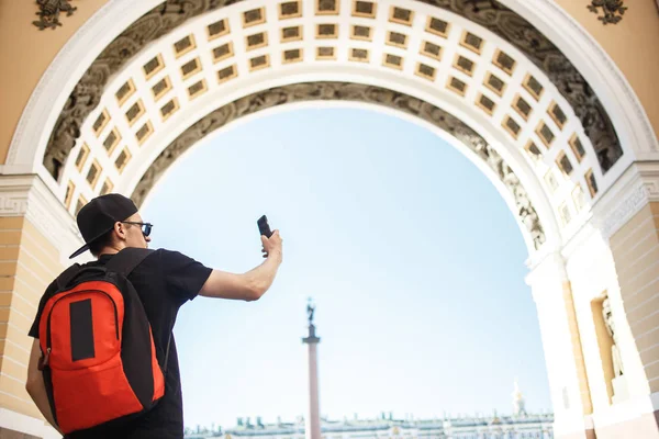 Joven turista con mochila tomando fotos móviles en la plaza del palacio en San Petersburgo —  Fotos de Stock