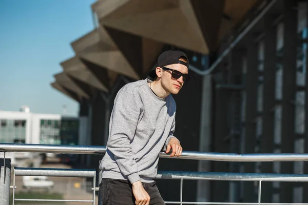 Bonito homem viajante no aeroporto moderno. Vestiu-se de óculos de sol redondos, boné preto e camisola cinza. — Fotografia de Stock