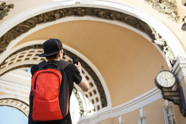 Молодой турист с рюкзаком фотографирует историческую арку здания Генштаба на Дворцовой площади в Санкт-Петербурге — стоковое фото