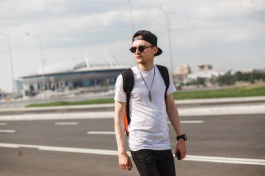 Şık adam turist bulanık futbol stadyumu arka plan üzerinde sokakta. Riund güneş gözlüğü ile siyah kot pantolon, siyah gömlek, siyah şapkalı giymiş. Kavramı hayranları, futbol, futbol maçları