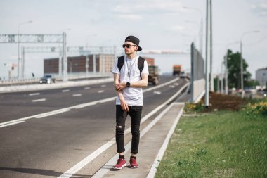 Şık adam otostopçu cadde veya otoyol üzerinde. O siyah kot pantolon giyiyor, siyah gömlek, siyah kapaklı yuvarlak güneş gözlüğü