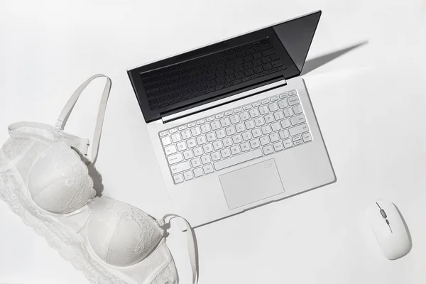 Erotic chat, virtual sex concept. White bra thrown on a modern laptop, against a white background. Minimalistic Flat lay, top view