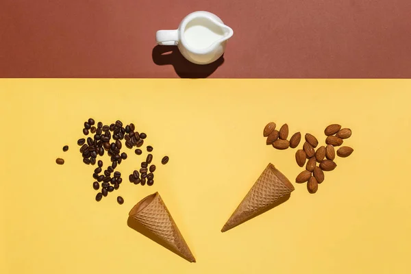 Conceito de preparação para sorvete ou café gelado. Jarro de creme, duas xícaras de waffle, grãos de café espalhados e amêndoas na mesa marrom amarela. Flat lay mockup — Fotografia de Stock