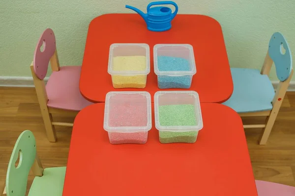 Cajas sensoriales de arco iris para niños pequeños con arroz colorido sobre una mesa roja. Kit educativo universal en jardín de infantes . —  Fotos de Stock
