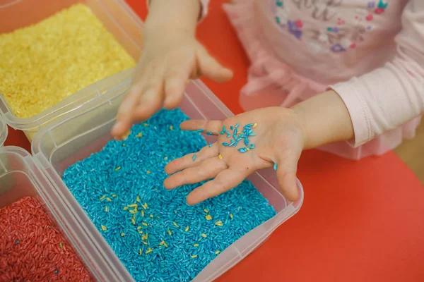 सेन्सर बॉक्समध्ये रंगीत तांदूळ खेळत मुलाचे हात. मुलांचे संवेदनशील शैक्षणिक किट — स्टॉक फोटो, इमेज
