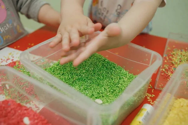 Детские руки играют с цветным рисом в сенсорной коробке. Набор сенсорных учебных материалов для младенцев — стоковое фото