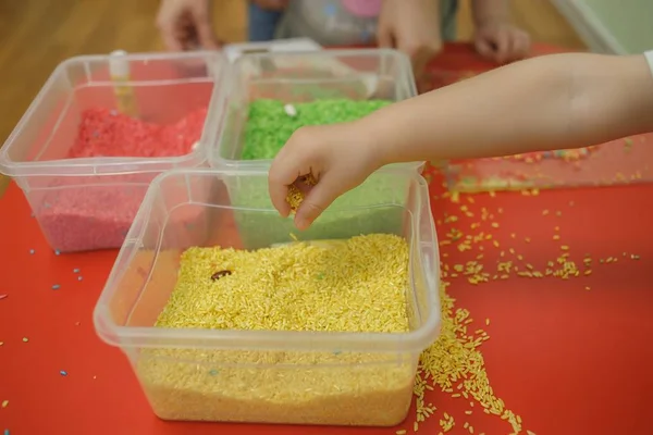 Детские руки играют с цветным рисом в сенсорной коробке. Набор сенсорных учебных материалов для младенцев — стоковое фото