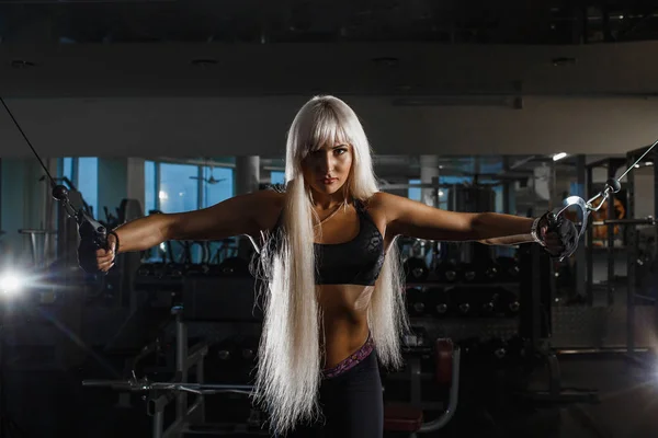 Entrenamiento de deportista muscular joven con simulador de bloque en el gimnasio, trabajando duro para los músculos fuertes del brazo. Chica mirando hacia adelante empujando las manos a los lados . — Foto de Stock