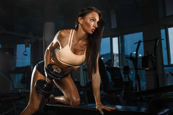 Sidovy av ung sportig tjej lyfta hårt hantlar på bänk i gymmet. — Stockfoto