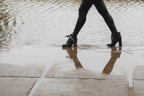The girl in leather boots going on a big puddle in the city. Water Splashes from boots. Autumn or spring cold wet weather concept