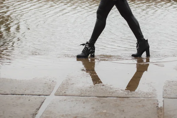 La ragazza con gli stivali di pelle che va su una grande pozzanghera in citta '. Schizzi d'acqua dagli stivali. Autunno o primavera freddo bagnato concetto — Foto Stock