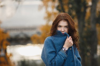 Sonbahar parkta poz sıcak Mavi paltolu Trendy genç kadın. O elleri tarafından mantoyu kapanış