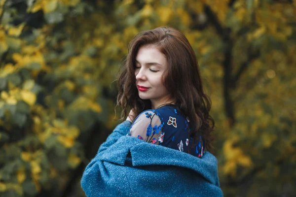 Cute young woman in blue coat and blue dress enjoying nature in the autumn park. Beautiful background cover of yellow leaves — Stock Photo, Image