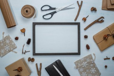 Siyah çerçeve ve Noel dekorasyon üstten görünüm. Noel hediyesi, makas, kalem, Hediyelik Çanta, çam kozalakları, çam dalları, ahşap beyaz mavi zemin üzerine meşe palamudu ile defter. El yapımı mockup, davet veya