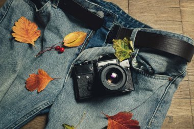 Sonbahar yaprakları, retro kamera ve ahşap zemin üzerine mavi jeans bileşimi. Üstten görünüm, düz yatıyordu. Tonda sıcak. Sonbahar fotoğraf çekimleri kavramı