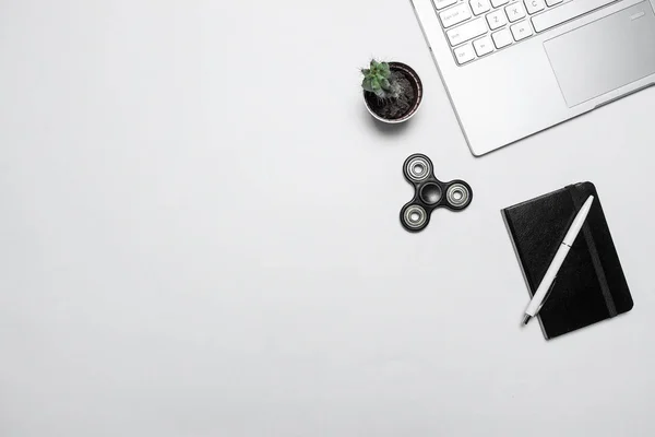 Minimal modern workspace. Composition with laptop, cactus, notebook with pen and fidget spinner on white desk. Top view, flat lay.
