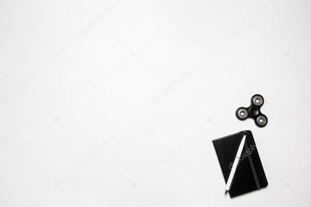 Modern minimalistic office or freelance workspace. Top view. Copy space. Flat lay. Composition with diary with pen and fidget spinner on white desk