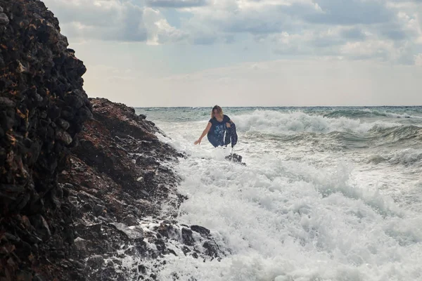 在狂风暴雨的海面上, 女游客带着巨浪、飞溅和泡沫爬上岩石。绝望和危险的行为 — 图库照片