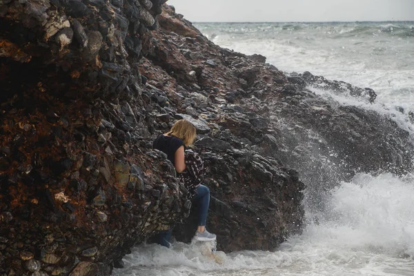 在狂风暴雨的海面上, 女游客带着巨浪、飞溅和泡沫爬上岩石。绝望和危险的行为 — 图库照片