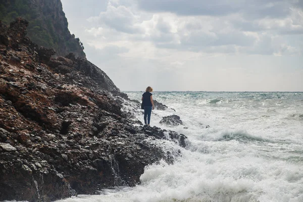 在狂风暴雨的海面上, 女游客带着巨浪、飞溅和泡沫爬上岩石。绝望和危险的行为 — 图库照片