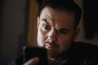 Sakallı adam amazedly karanlık odada smartphone için arıyorum. Yakın çekim.