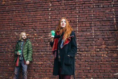 Kış tatil, dating, moda ve ilişki kavramı. Şık çift iki bardak kahve kırmızı tuğla duvara poz