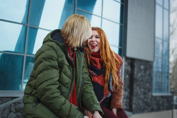 Молода пара європейських веселяться в міському тлі зими. Панки або брюки в обтяжку стиль. Руда дівчина одягнені в червоні шарф, коричневий пальто, короткі шорти і колготки. Блідий людина одягнені в зелені bolognese — стокове фото