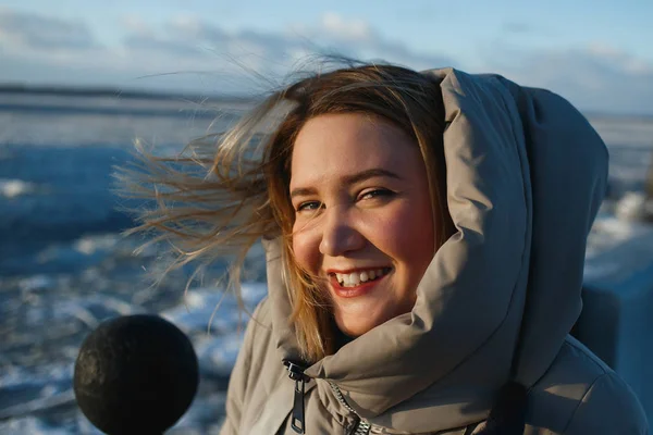 Портрет довольно веселой улыбающейся женщины на замерзшем речном фоне в солнечный зимний день. Здоровая зимняя ходьба в грешный морозный день — стоковое фото