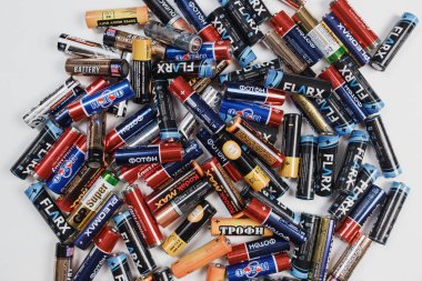 Arkhangelsk, Russia, December 3, 2018: A lot of alkaline batteries scattered on a white table. Concept of recycling, utilization issues clipart