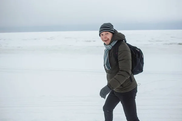 Stilvoller kaukasischer Mann, der an der schneebedeckten Küste wandert. er zeigt einen lustigen Gesichtsausdruck mit der Zunge, der Winterspaß, Urlaub, Tourismuskonzept ausbreitet. — Stockfoto