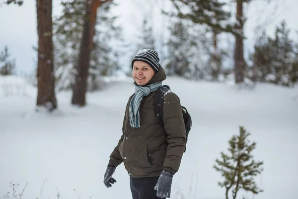 Porträt attraktiver Mann im winterlichen Kiefernwald. er bekleidet mit dunkelgrüner Jacke, grauem Schal, Mütze und Handschuhen — Stockfoto