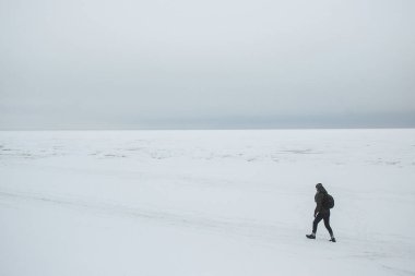 Yalnız adam uzun yürüyüşe çıkan kimse kış deniz kıyısında gidiş sırt çantası ile. Minimalist kompozisyon