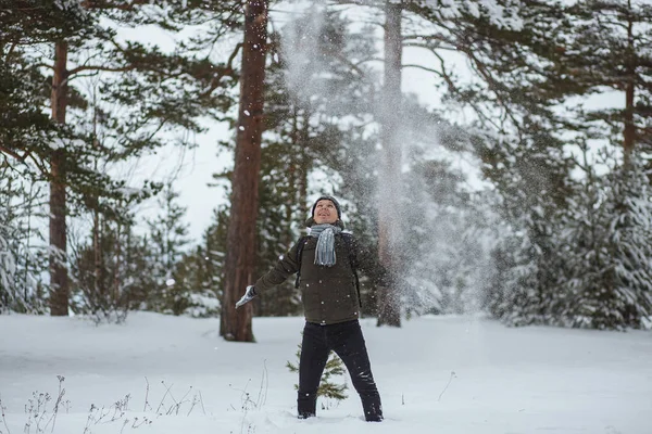Porträt fröhlicher Mann im winterlichen Kiefernwald. er bläst am Wintertag Schnee von den Handschuhen — Stockfoto