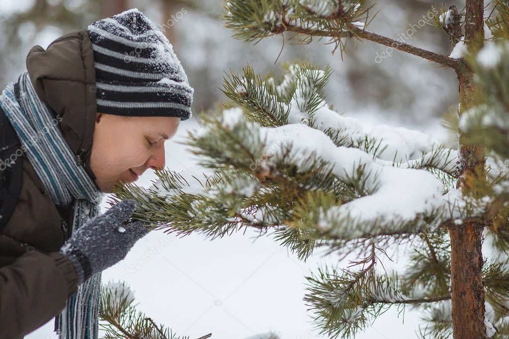 Young man sniffing a pine branch in winter forest. Concept of res, aromatherapy, healthy lifestyle, harmony with nature