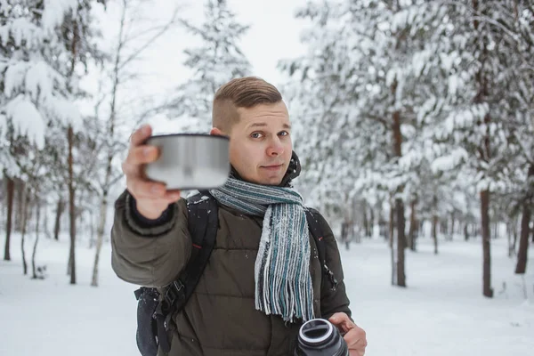 Stilvoller Mann mit einer Thermoskanne heißen Tees in einem schneebedeckten Nadelwald — Stockfoto