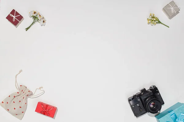 Мінімалістична плоска композиція з ретро-камерою, червоно-блакитними подарунковими коробками, полотняною сумкою з червоними формами серця та весняною квіткою на білому тлі. Модний плоский макет для блогерів — стокове фото